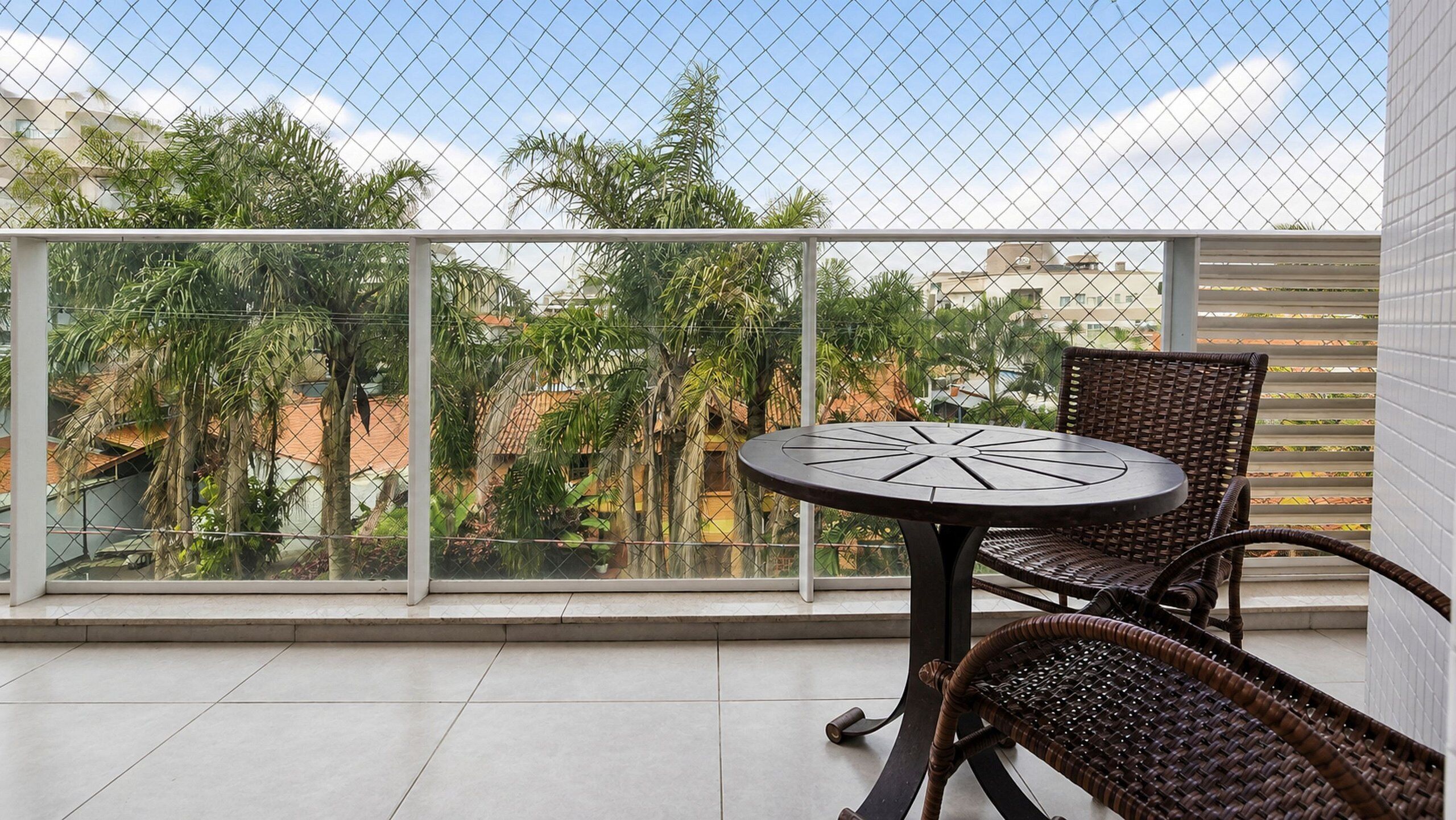 A balcony with a glass railing, a round table, and two wicker chairs.