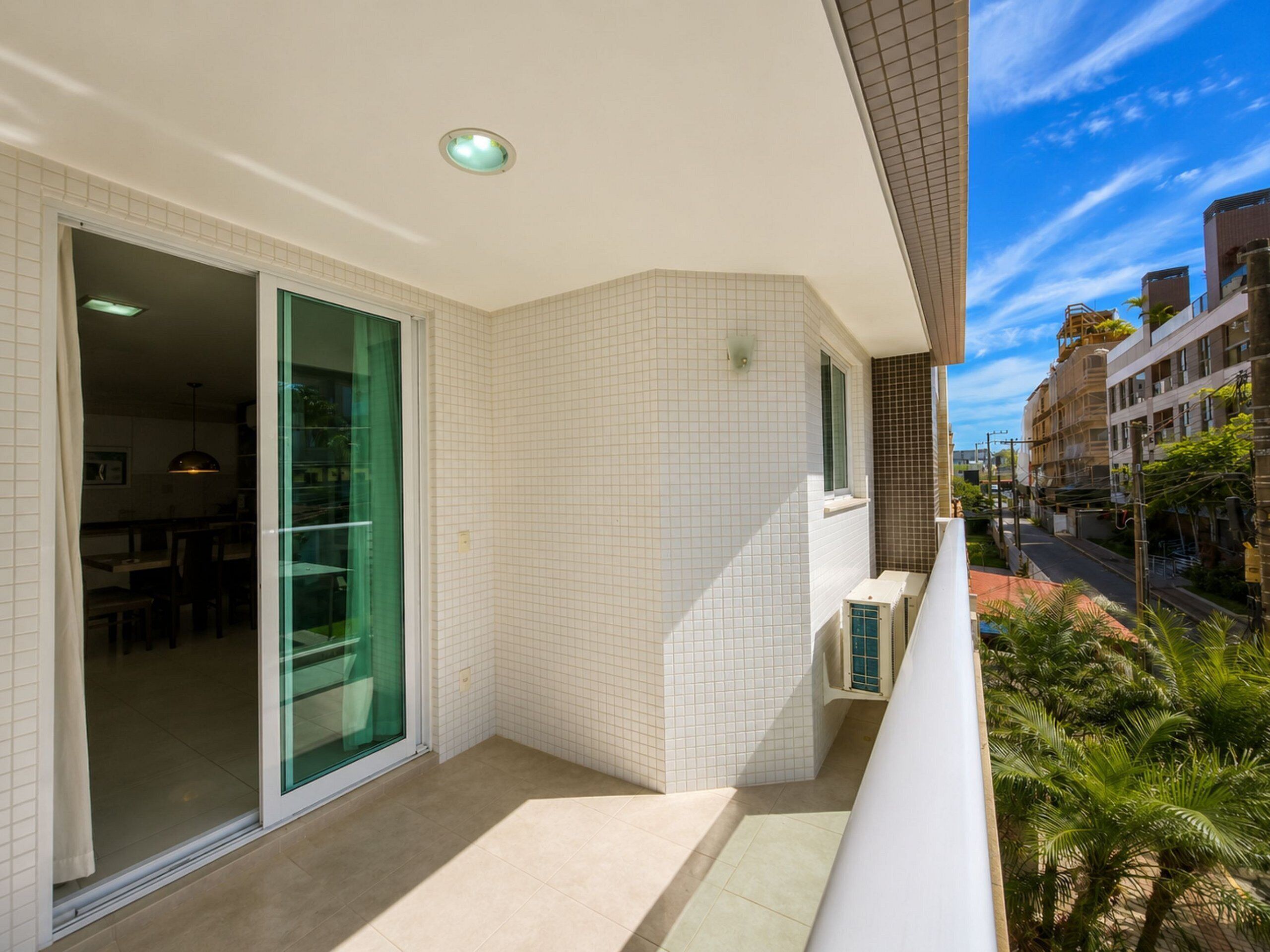 A modern residential building with a balcony, large sliding glass doors, and a view of the street and neighboring buildings.