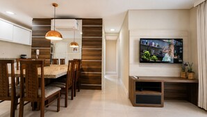 Un soggiorno moderno con zona pranzo, televisione a schermo piatto e cucina sullo sfondo.