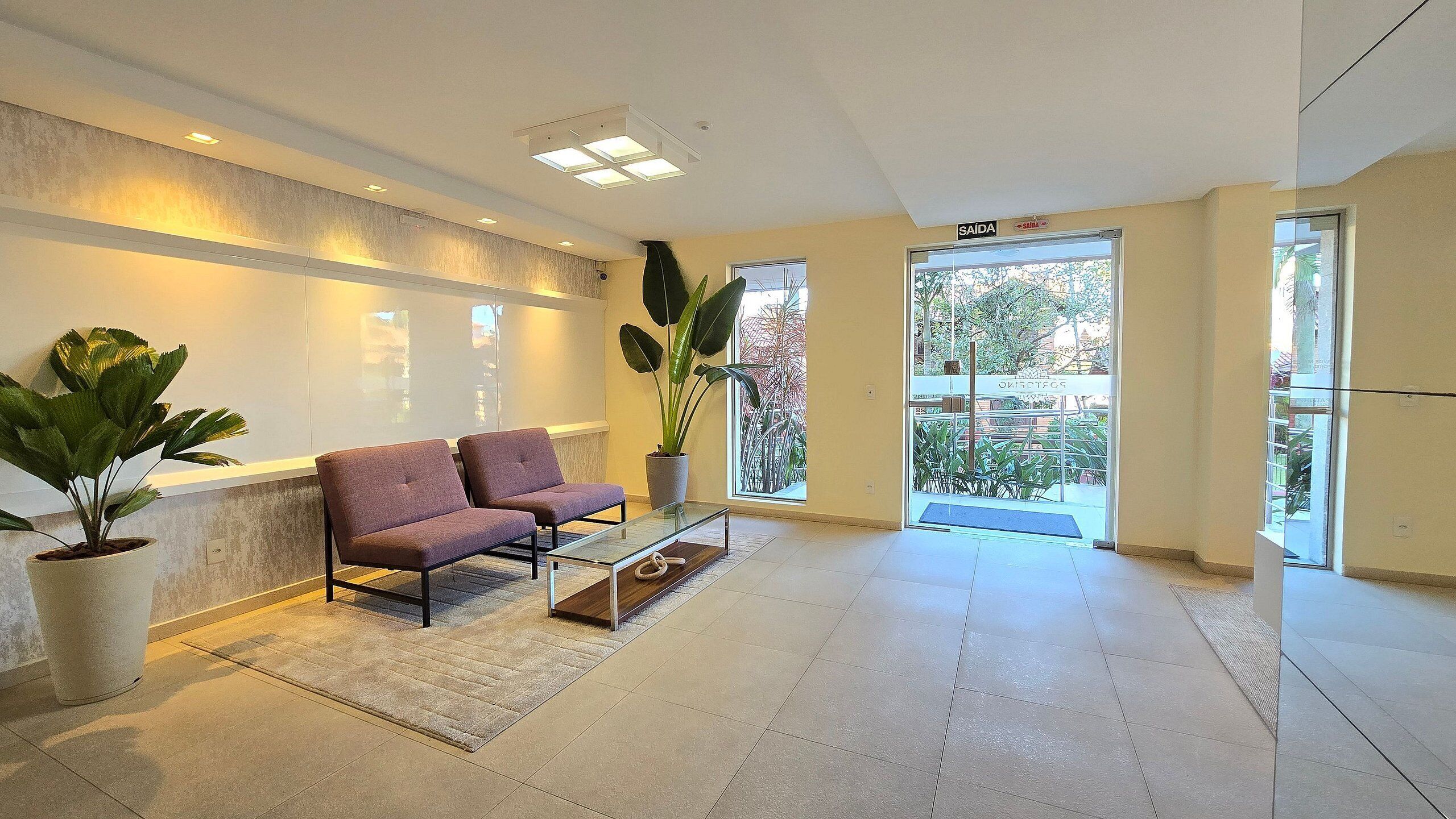 A reception area with two armchairs, a glass coffee table, potted plants, and a view of the outside.