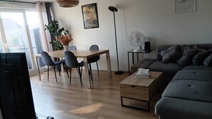 A modern living room with a grey sofa, a wooden dining table with four chairs, a standing floor lamp, and a painting on the wall. - An air-conditioned haven of peace, a 2-room apartment just a stone's throw from Paris (Choisy-le-Roi)