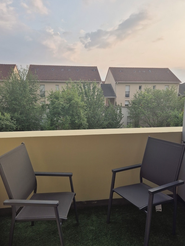 A balcony with two chairs, a yellow wall, and a view of residential buildings.
