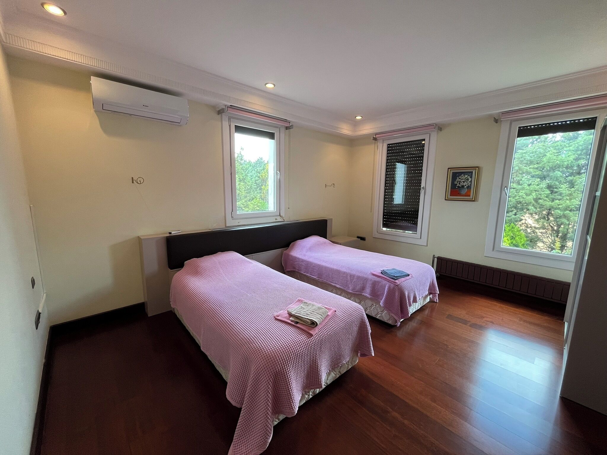 A bedroom with two beds, a window with blinds, a radiator, and a picture on the wall.