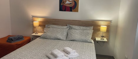 A neatly made bed with patterned bedding and towels, two bedside lamps, and a painting on the wall.