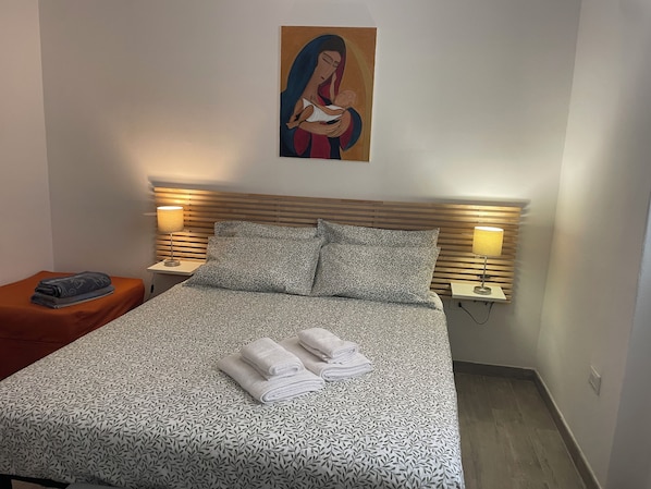 A neatly made bed with patterned bedding and towels, two bedside lamps, and a painting on the wall. - Elegant fully-equipped apartment in the heart of Palermo. No congestion charges. (Palermo)