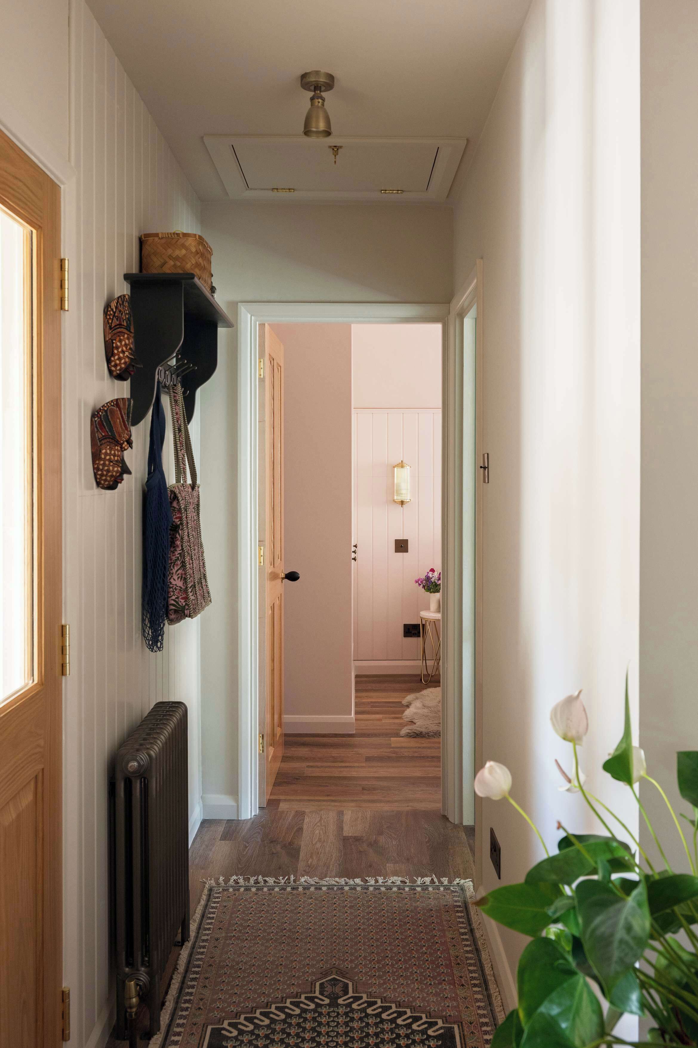 Un couloir avec un radiateur, un tapis à motifs et des chapeaux accrochés au mur.