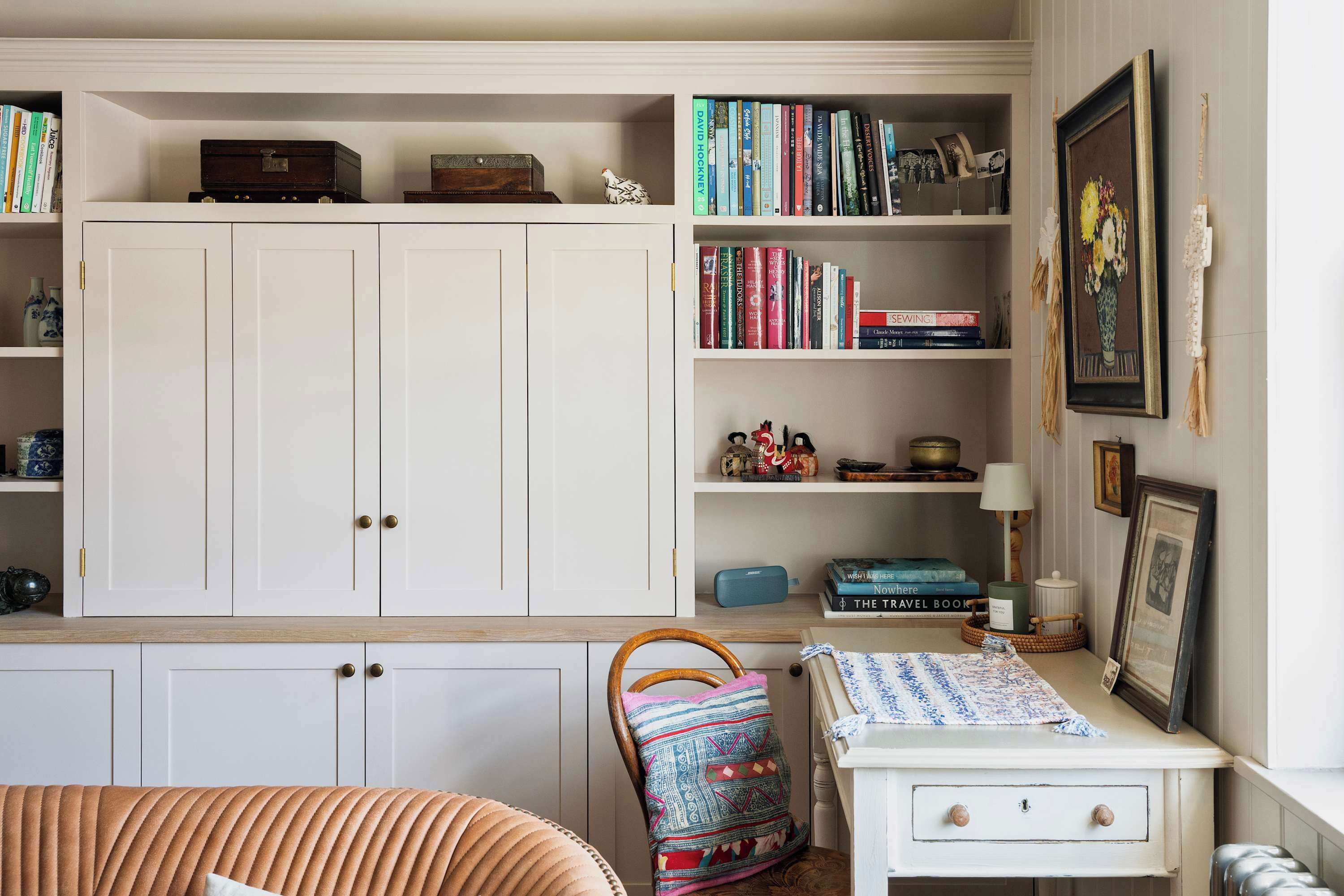 Une pièce comprenant une grande armoire blanche, une petite table blanche avec une lampe et une chaise agrémentée d’un coussin coloré.