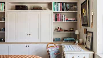 Une pièce comprenant une grande armoire blanche, une petite table blanche avec une lampe et une chaise agrémentée d’un coussin coloré.
