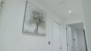 Een hal met een schilderij van een boom aan de muur, een deur en een lamp aan het plafond.