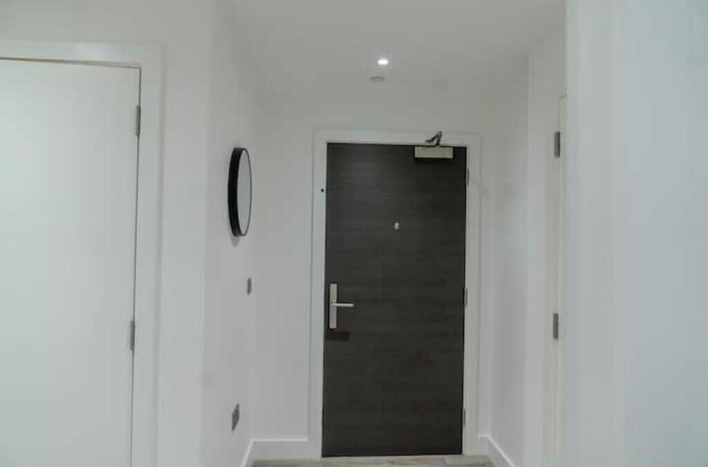 A hallway with a closed door, a wall-mounted mirror, and a ceiling light.