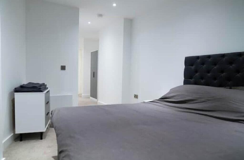 A bedroom with a bed, a nightstand, and a door leading to another room.