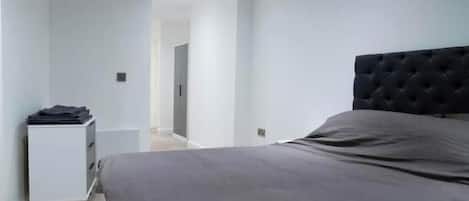 A bedroom with a bed, a nightstand, and a door leading to another room.