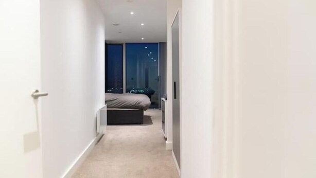 A narrow hallway leading to a bedroom with a bed and a window. - Stylish High-Rise Apartment with Skyline Views | Deansgate, Manchester (Manchester)