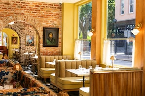 A restaurant interior with brick walls, wooden furniture, and large windows. - The Jardin (Savannah)