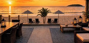 A beachside seating area with lounge chairs and tables, overlooking the ocean at sunset. - The Palms Beach House Milford (Milford)