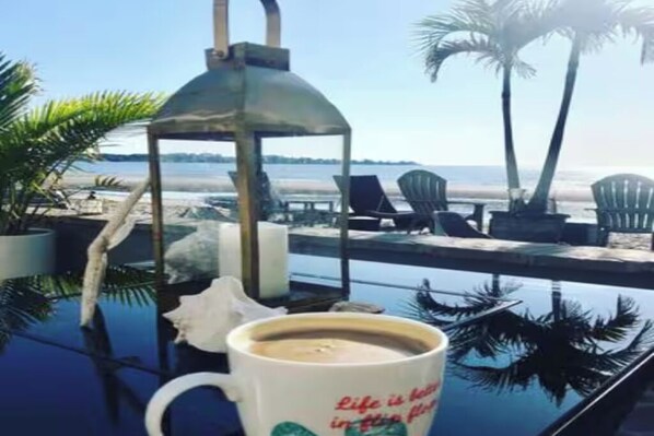 Vista despejada de un área de piscina frente al mar, con sillas de descanso y una palmera.