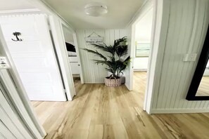 A hallway with wooden flooring, white walls, and a potted plant. - The Palms Beach House Milford (Milford)