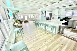 A modern kitchen with bar stools, a dining area with chairs, and a large island. - The Palms Beach House Milford (Milford)
