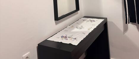 Un baño con un tocador negro, un espejo, un estante con un reloj y una planta, y una cortina a rayas negras y blancas.