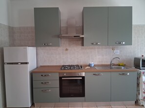 Een keuken met een gasfornuis, oven, spoelbak en een koelkast.
