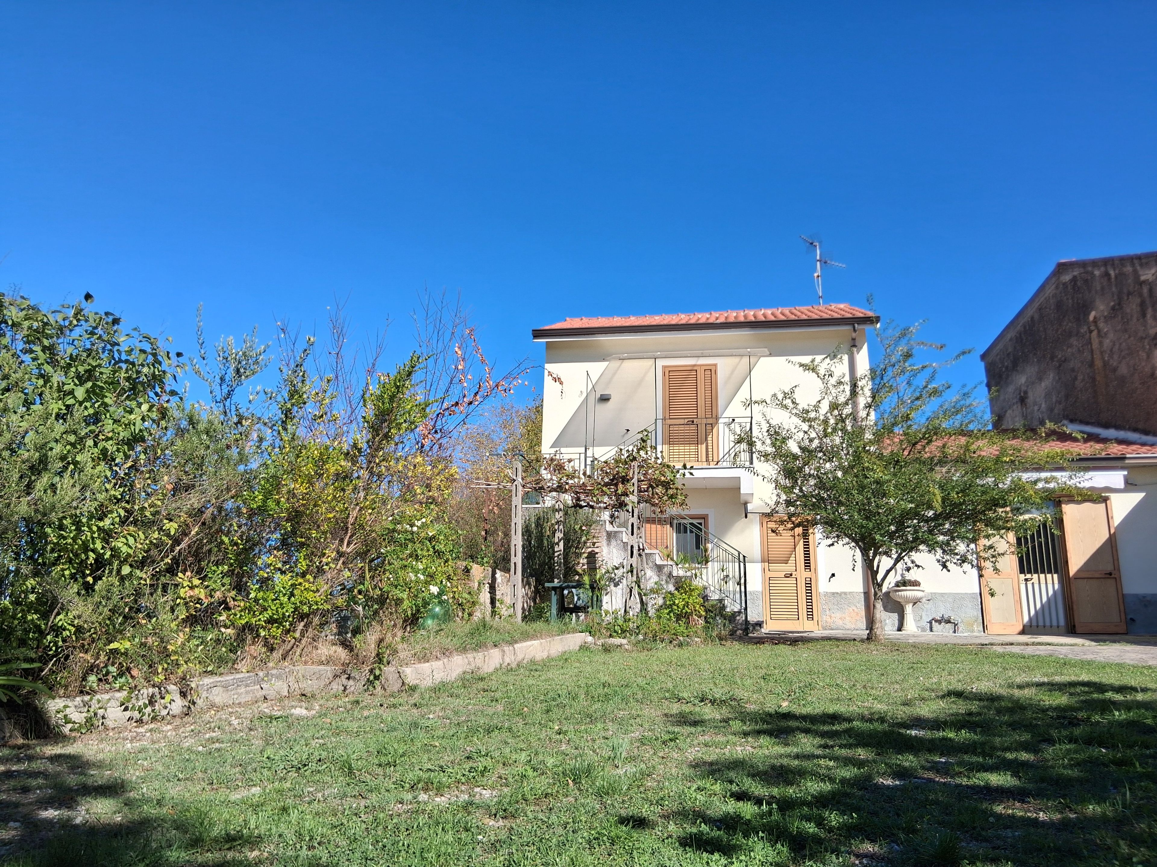 A two-story building with a red-tiled roof, a small garden, and a stone wall.