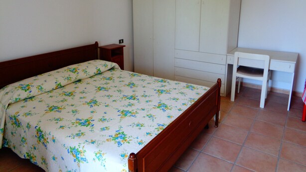 A bedroom with a bed, a wardrobe, a nightstand, and a desk.