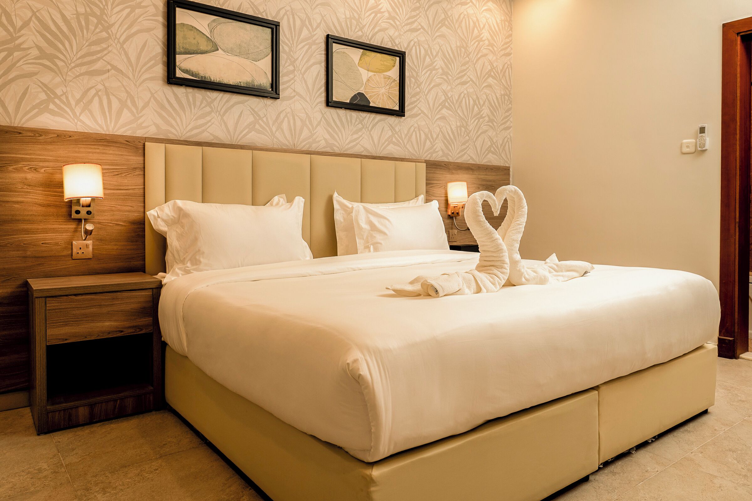 A hotel room with a large bed, two wall-mounted lamps, and a framed artwork above the bed.