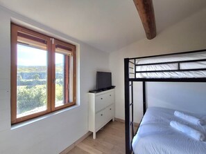A bedroom with a bunk bed, a window with a view of greenery, a white dresser with a flat-screen TV, and a wooden ceiling beam. - Nature, waterfall & jacuzzi (Berlou)