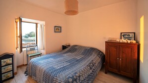 A bedroom with a bed, a wooden cabinet, a chair, a small table, a picture on the wall, and a window with curtains. - One of a kind! Ground-floor apartment with a terrace overlooking the sea (Carnac)