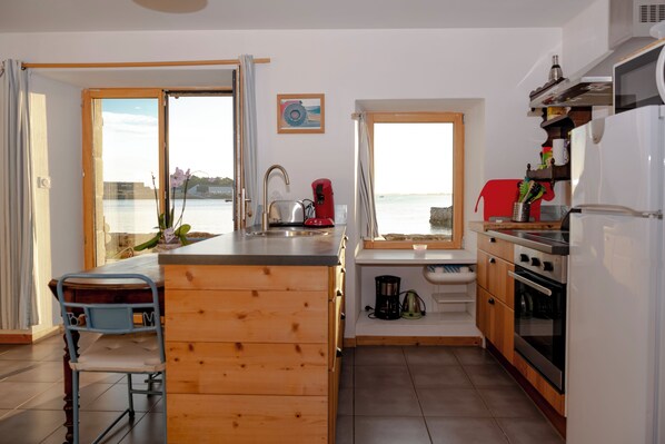 Eine moderne Küche mit Holzschränken, einer Edelstahl-Spüle und Meerblick durch große Fenster.