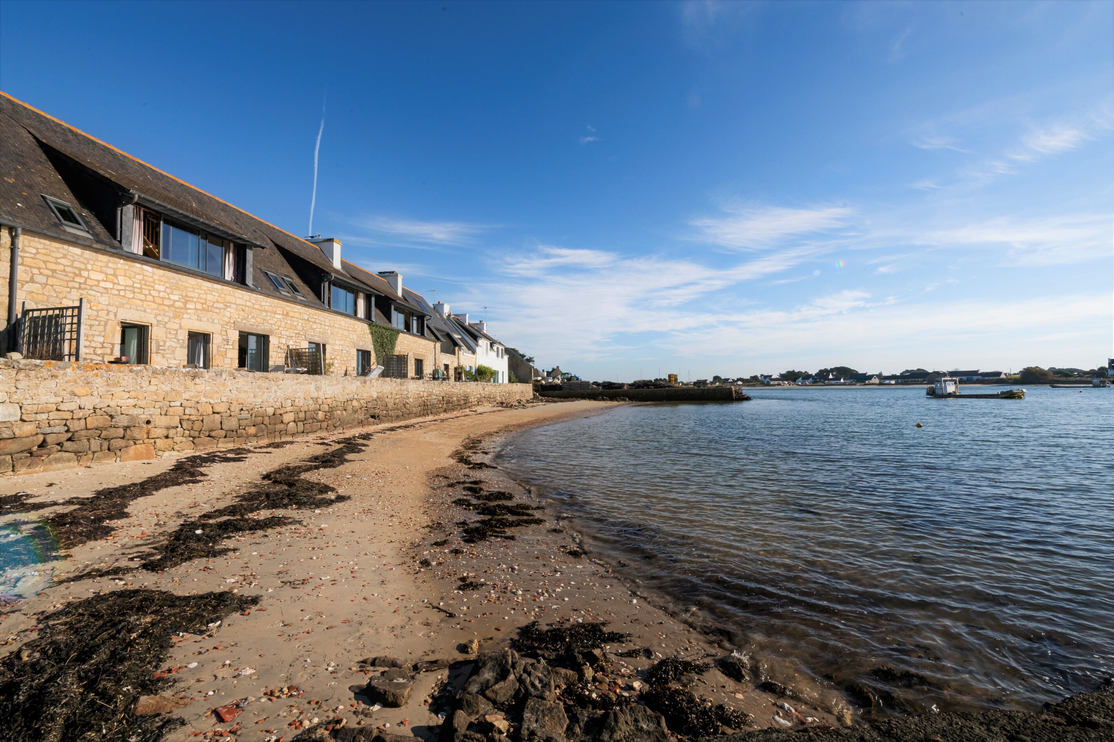 A coastal building with stone walls and multiple windows, adjacent to a sandy beach with seaweed and debris.