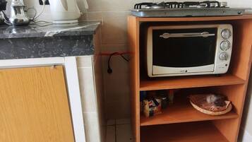 A kitchen with a microwave on a wooden shelf, a kettle, and a gas stove.