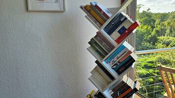 Ein Bücherregal mit Büchern, ein gerahmtes Schild an der Wand und ein Blick auf Grünflächen im Freien.