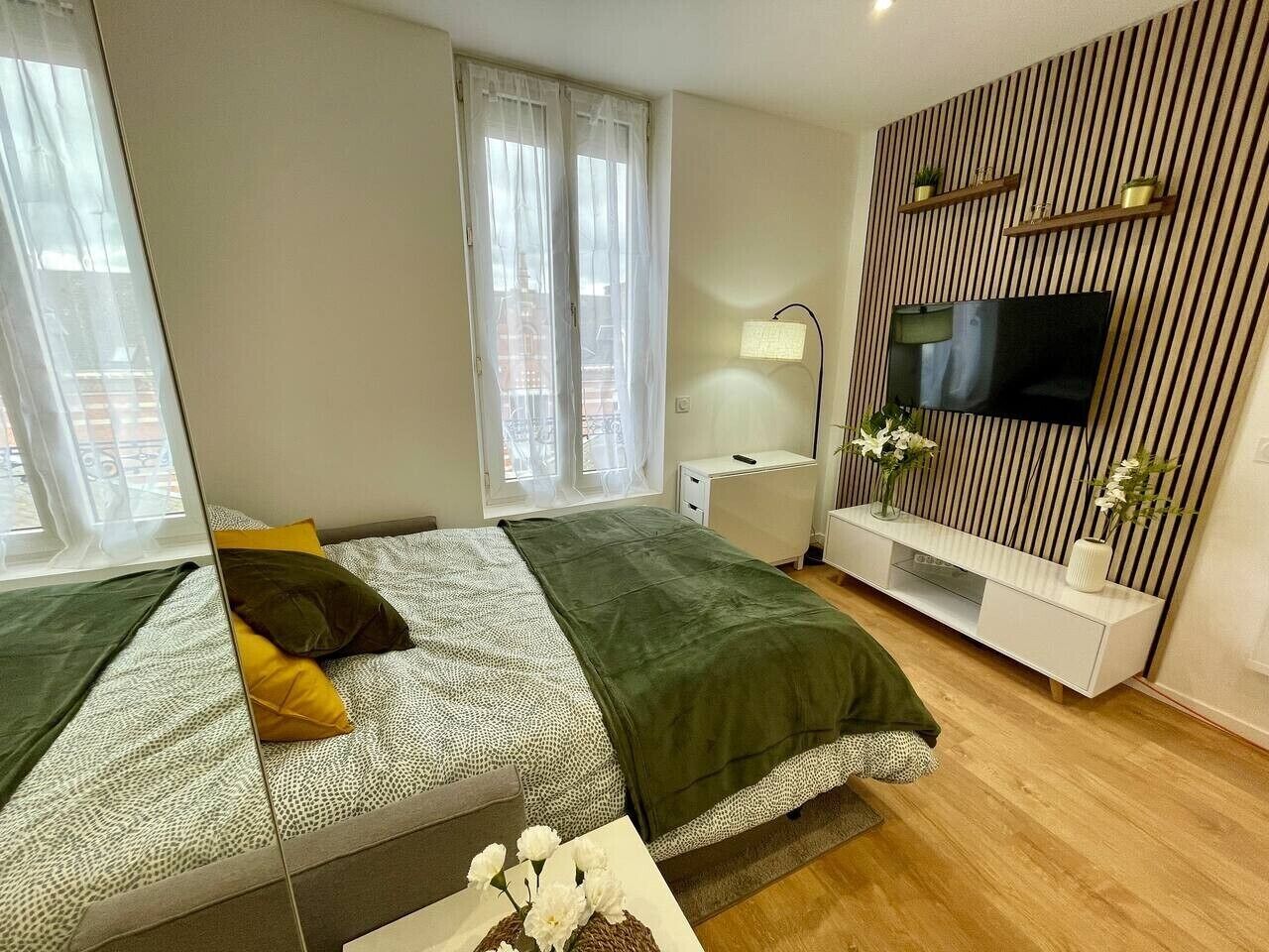 Ein modernes Schlafzimmer mit einem Bett, einem Fernseher, einem Nachttisch und einem Fenster mit Vorhängen.