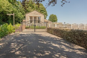 A gated entrance to a stone building with a traditional design, surrounded by greenery and a stone wall. - The old School House Sleeps 16 (Barnoldswick)