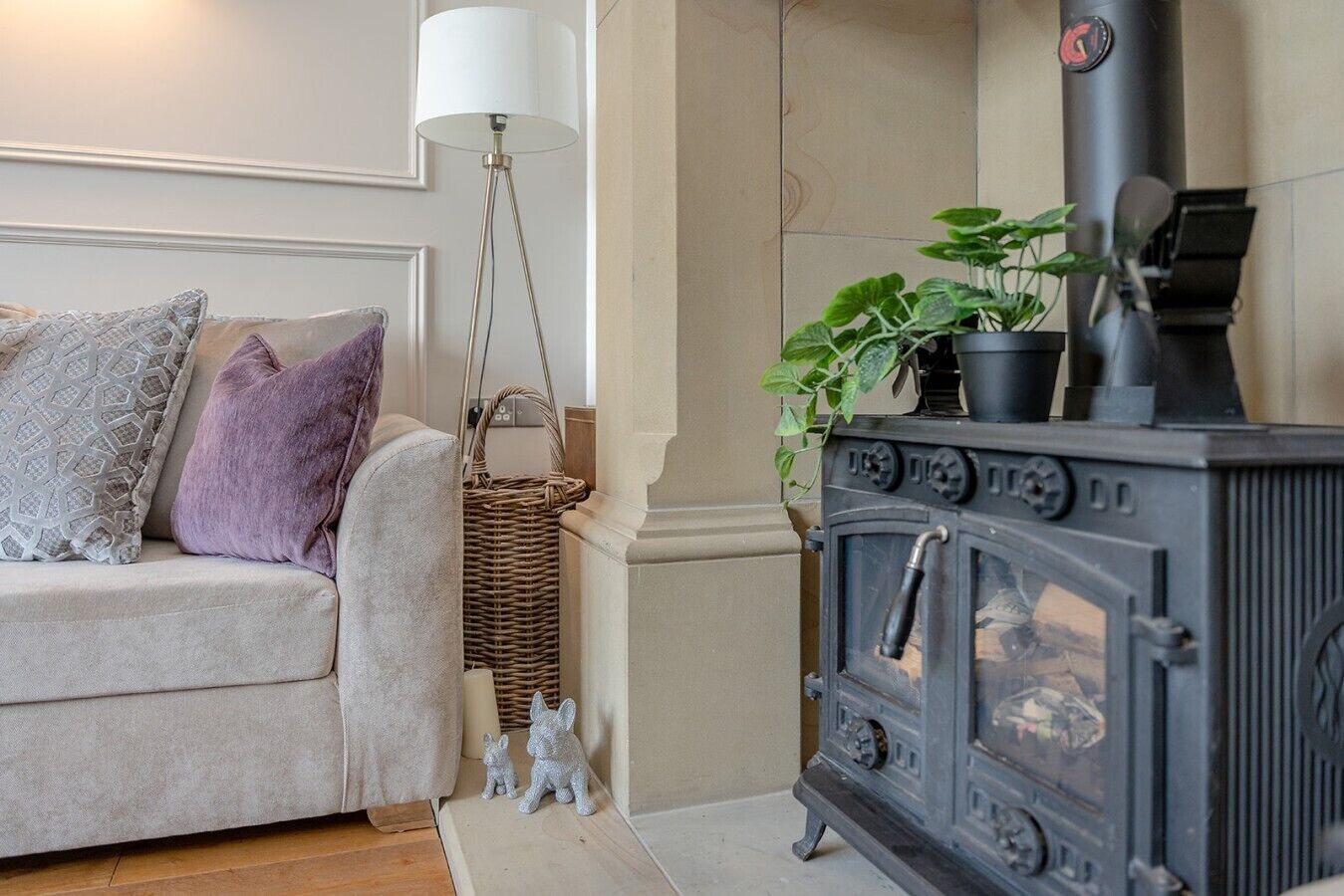 A cozy living room with a sofa, a lamp, a wicker basket, a small rabbit figurine, and a black wood-burning stove.