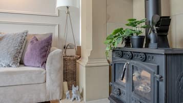 A cozy living room with a sofa, a lamp, a wicker basket, a small rabbit figurine, and a black wood-burning stove.