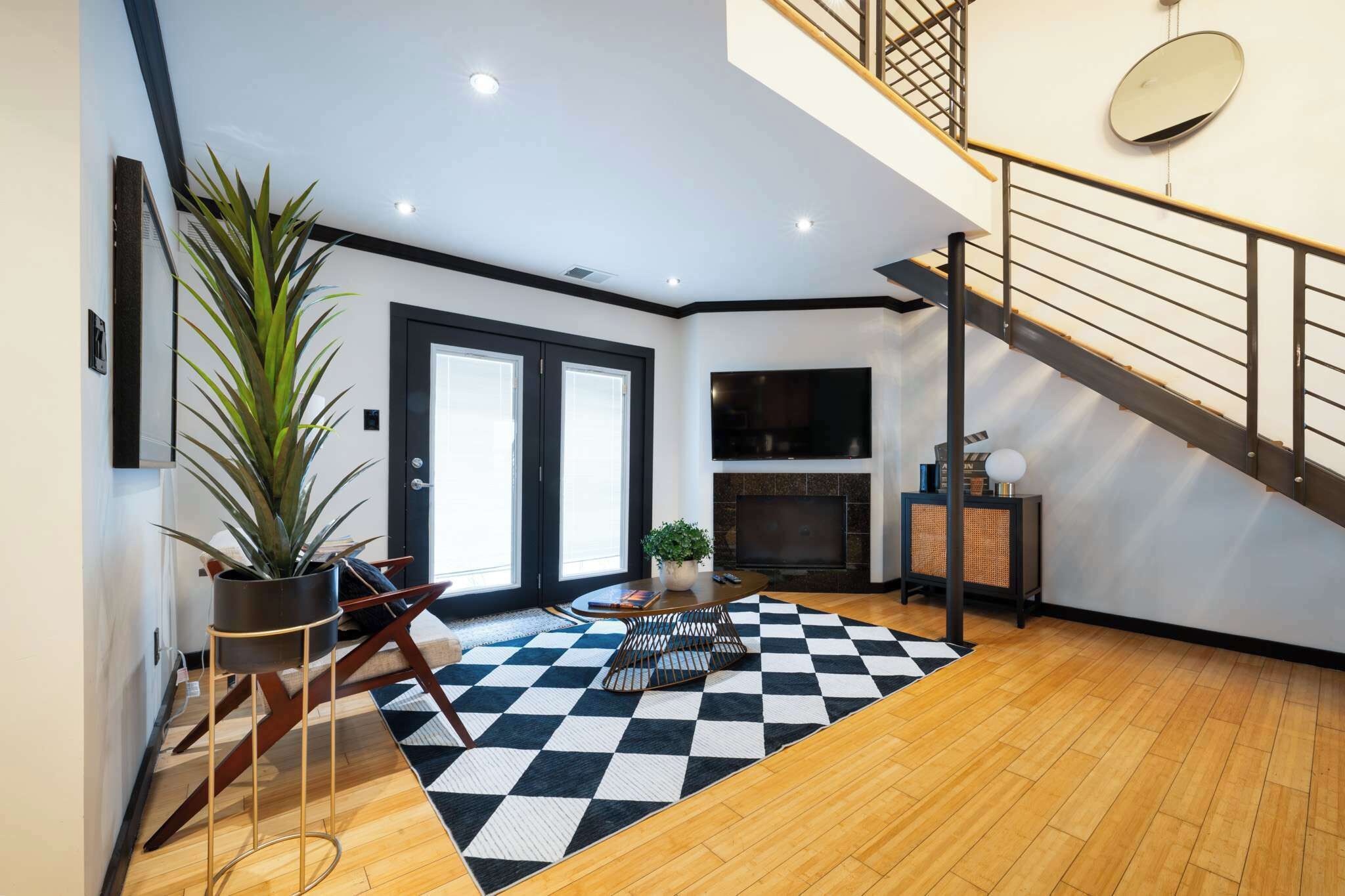 Een moderne woonkamer met een zwart-wit kleed, een bank, een salontafel, een open haard en een trap.