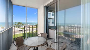 A balcony with a table and chairs, overlooking a beach and a parking area.