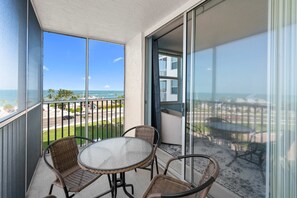 Un balcón con mesa y sillas, con vista a una playa y un estacionamiento.