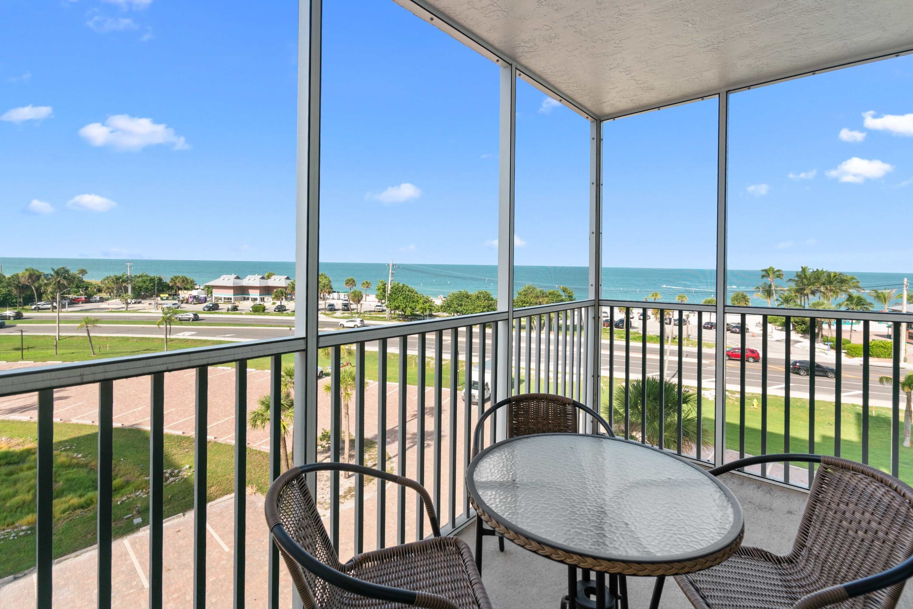 A balcony with a view of the ocean, a table, and two wicker chairs.