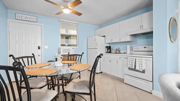 A kitchen with white cabinets, a glass dining table, and a ceiling fan.