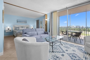 A modern living room with a glass coffee table, a sofa, and a view of a balcony with outdoor furniture.