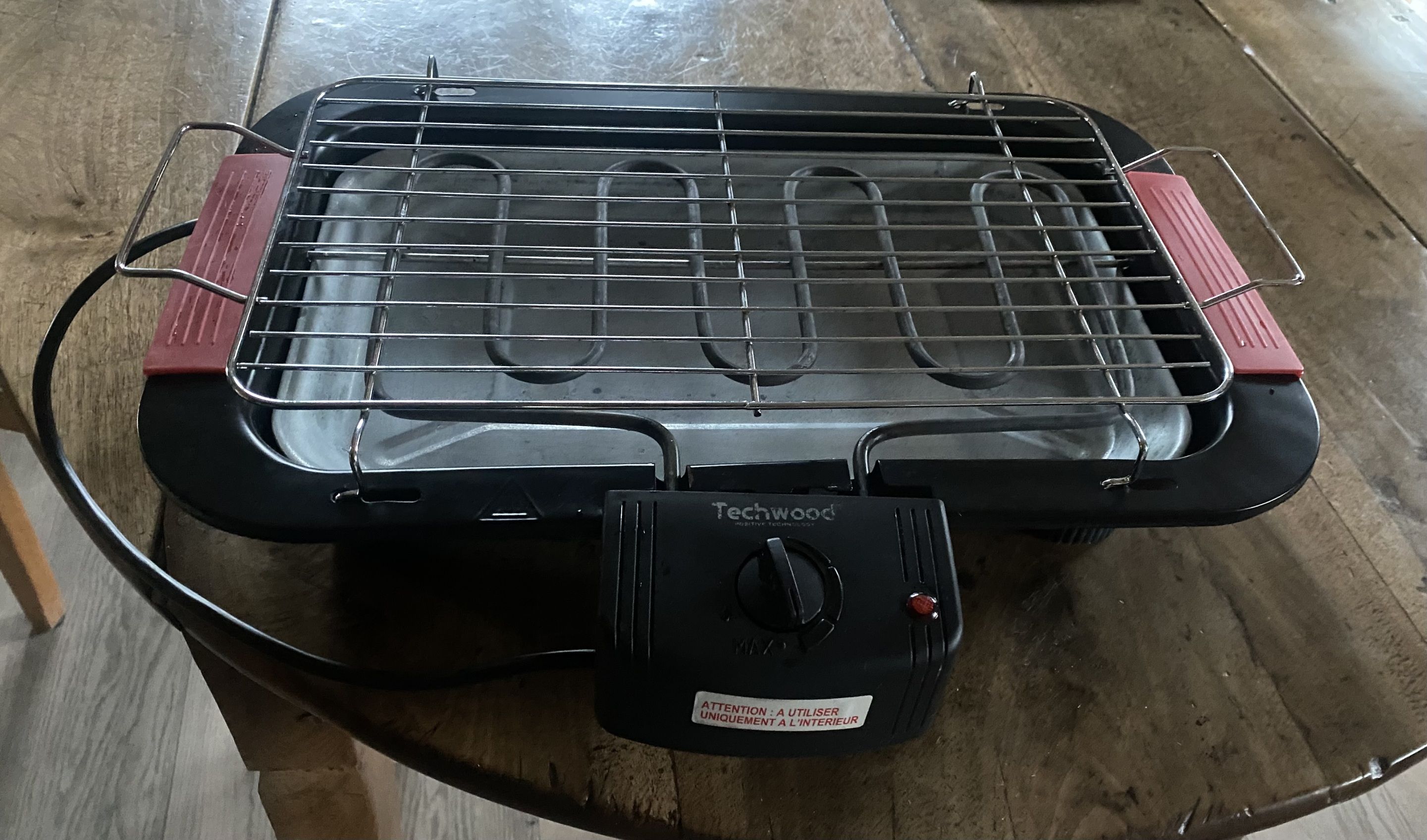 A portable grill with a control knob and a safety label.