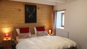 A bedroom with a wooden headboard, a bed with white bedding, two red pillows, a nightstand with a lamp, and a window with curtains.