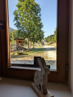 Vista desde una ventana a un paisaje rural con una hamaca, una pequeña construcción de madera y un cielo despejado.