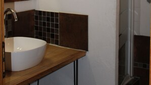 A bathroom with a wooden vanity, a white sink, a mirror with a wooden frame, and a tiled shower area.