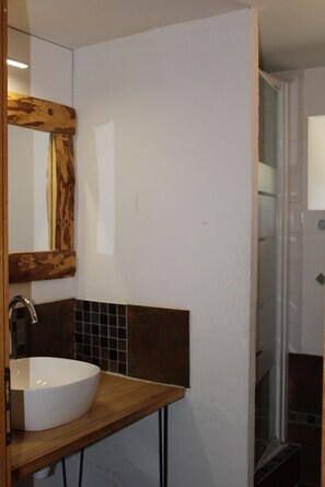 A bathroom with a wooden vanity, a white sink, a mirror with a wooden frame, and a tiled shower area.