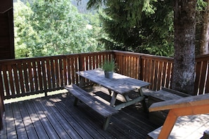 A wooden deck with a picnic table and benches, surrounded by trees.