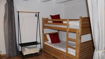 Ein Schlafzimmer mit Etagenbett, Holzrahmen, Ablagefläche unter dem unteren Bett und einem Vorhang links.